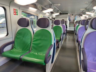 Interior of modern train carriage featuring vibrant green and purple seating, showcasing contemporary design and spacious layout with copy space