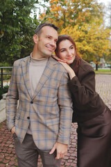 Happy smiling couple embracing and leaning heads together, showing affection on a brick path surrounded by autumn trees