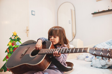 A little girl is learning to play an acoustic guitar 