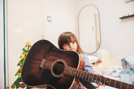 A little girl is learning to play an acoustic guitar	