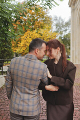 Romantic couple embracing and touching foreheads, sharing a private moment on a cobblestone path near vibrant yellow autumn trees