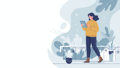 Happy woman in warm sweater using a digital tablet outside during winter snowfall