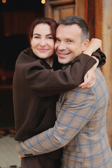 Close-up portrait of a happy, stylish couple embracing tightly and smiling at the camera in warm autumn jackets