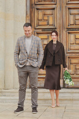 Elegant couple posing and showing affection on stone steps in front of a massive ornate wooden door of a historic building