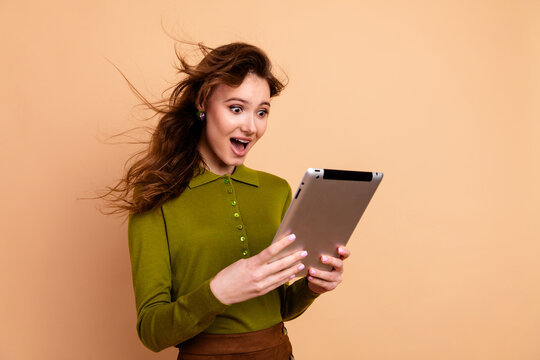 Young woman in olive green sweater reacts with joyful surprise while using a tablet against beige background suitable for lifestyle shopping