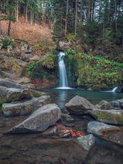 wide angle portrait view to waterfall in dark forest with stones