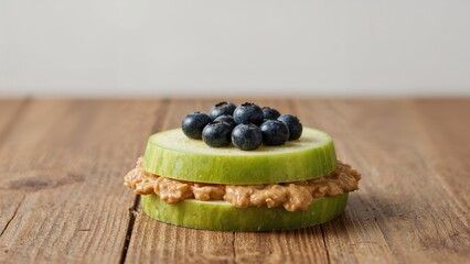 Slices of cucumber with hummus and blueberries on top placed on a wooden surface. Fresh, healthy snack. Vegetarian food. Simple and nutritious.