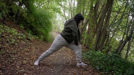 outdoor fitness move, side lunges among lush green trees, woman performing balanced side lunge on wooded trail, engaging in mobilityenhancing workout amid forested landscape with proper gear
