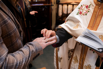 Close-up of a priest placing a golden wedding ring onto the finger of the groom during a traditional orthodox christian marriage ceremony