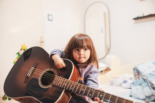 A little girl is learning to play an acoustic guitar 
