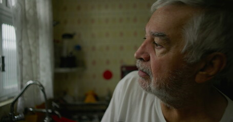 Close-up of elderly man in kitchen with introspective expression, representing solitude, aging, and moments of quiet reflection in domestic life