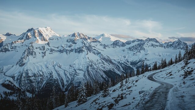 Snow-covered mountains and a winding road through the forested terrain. Landscape and mountain scenery. Nature and wilderness. The scene of snowy peaks and alpine environment.