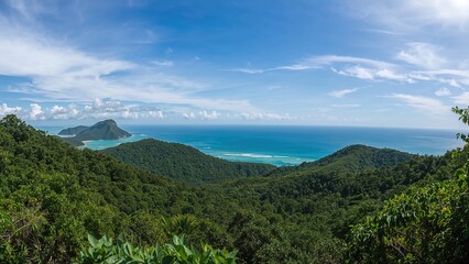 Lush green forested hills leading to ocean views under a blue sky with clouds.