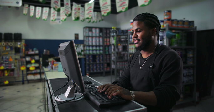 Side view of young man working at a computer in a paint store, smiling and engaging with technology, representing modern retail operations and attentive service