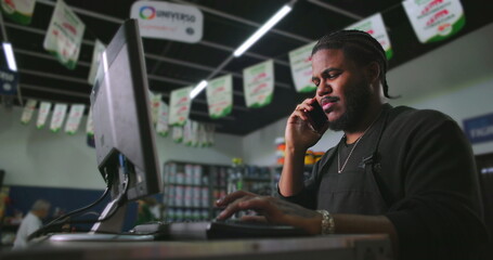 Young man working at a counter in a paint store, talking on the phone while using a computer, representing multitasking, professionalism, and efficient customer service