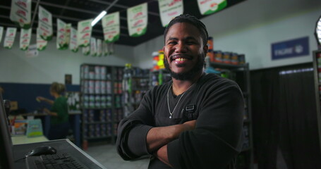 One Black male retail employee with arms crossed, confidently standing at counter, shop interior visible, engaging and professional customer service approach