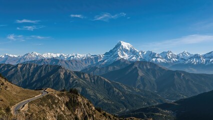 Snow-capped mountains in the Himalayas with a winding road through green hills, under a clear blue sky.
