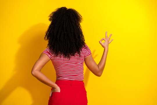Young fashionable woman in striped top posing against vibrant yellow background with a cheerful ok gesture symbolizing positivity.