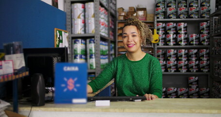 Female entrepreneur sitting at a desk in a hardware store, smiling confidently while working, surrounded by shelves of paint and supplies in a professional setting