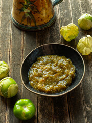 A bowl with famous Mexican salsa of roasted tomatillos and toasted chilies de árbol pounded with a mortar and pestle—fresh tomatillos on the rustic wooden boards.
