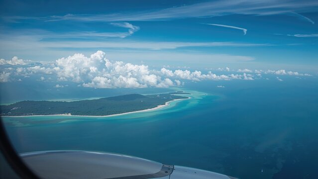 Aerial view of shoreline and ocean from an airplane window, with clouds and blue sky. Coastal landscape and water. Sky and clouds.