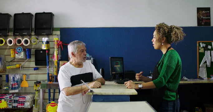 Shopkeeper attentively listening to an elderly customer at the counter in a hardware store, demonstrating patience and understanding in customer interaction
