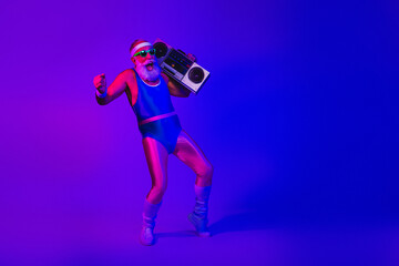 Elderly man in retro fitness outfit dances with a boombox under vibrant purple and blue neon studio lights