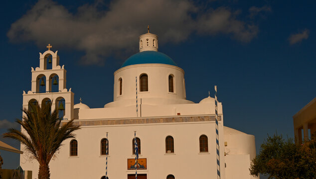 Close-up view of a traditional whitewashed Greek Orthodox church featuring a vibrant blue dome, arched windows, and classic Cycladic architecture under a clear Mediterranean sky. The minimalist compos