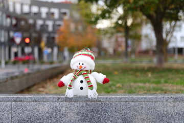 Snowman toy in a warm city, Christmas decoration in urban background, winter in warm country