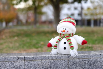 Snowman toy in a warm city, Christmas decoration in urban background, winter in warm country