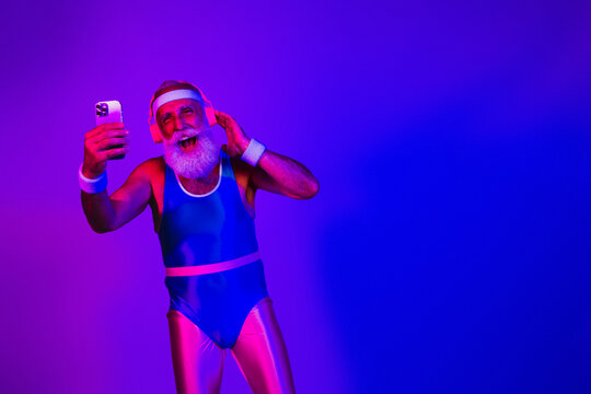 Energetic elderly man in neon retro jumpsuit dances with headphones taking a selfie for a festive fitness themed portrait