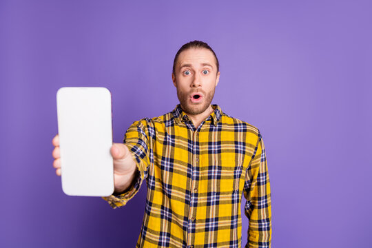 Young handsome guy in a yellow checkered shirt with blank smartphone purple background advertising fashion lifestyle promotion shopping brand