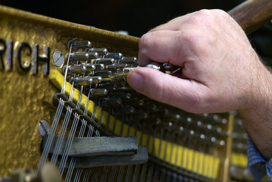 Piano tuning craftsmanship — the art of fine adjustment. Close-up of a piano tuner adjusting a vertical piano string with a handcrafted tuning lever.