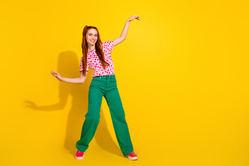 Young girl dancing in bright yellow studio wearing pink checkered shirt and green pants