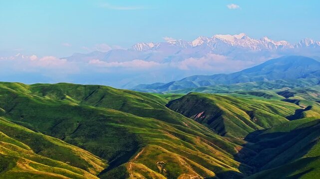 aerial hyper lapse of Kyrgyzstan green foothills with snowcapped mountains on the horizon at sunny summer day
