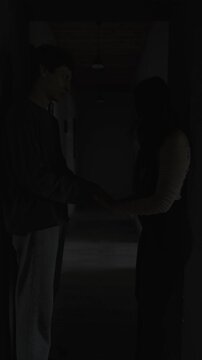 Guilt ridden boyfriend apologizing after argument holding girlfriend hands in dark hallway emotional tension and remorse Vertical Video