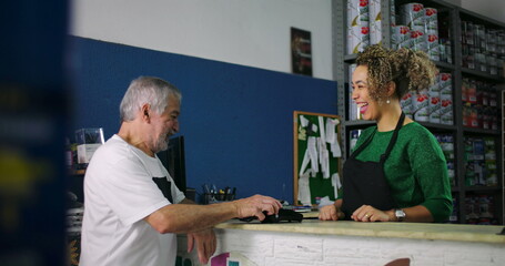 Smiling young woman and older man engaging in a light-hearted exchange during a transaction at a...