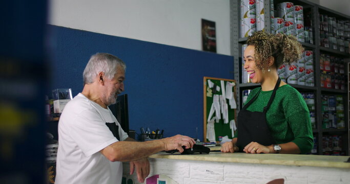 Smiling young woman and older man engaging in a light-hearted exchange during a transaction at a hardware store counter