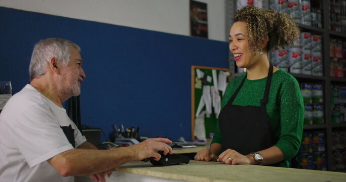 Smiling young woman assisting an older man at a hardware store counter during a transaction with a card machine