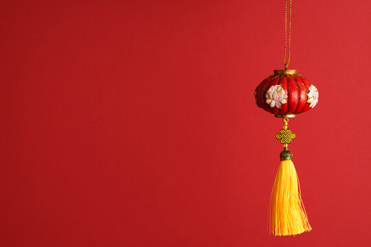 Chinese lantern ornament with white floral embroidery and a long golden yellow silk tassel, hanging against a vibrant red background for Lunar New Year or Spring Festival celebrations.