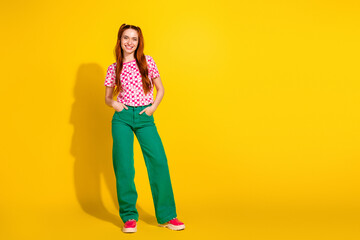 Young girl fashion model in checkered pink top and green pants standing against bright yellow background for lifestyle and shopping promotion