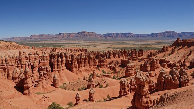 Red rock formations and cliffs in a desert landscape with a distant mountain range under a clear blue sky.