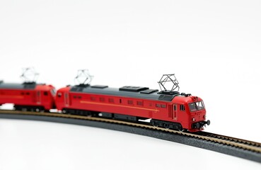 Red model trains run on tracks isolated on white. Miniature electric locomotives with pantographs are part of a railway diorama setup. Tiny transport collection for hobbyists.