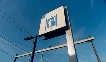 Blue elevator accessibility sign against clear sky with overhead catenary wires (this image was made with an anamorphic lens)