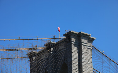 brooklyn bridge structure and the american flag flying above the cables