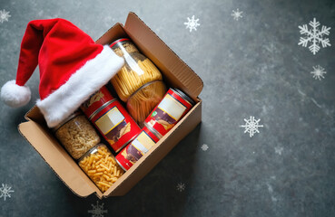 Cardboard box with pasta jars, canned goods and Santa hat. Food items for charity donation this holiday season. Christmas gift aid for needy families.