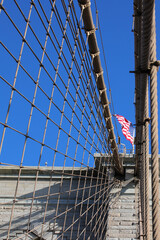 US flag waving amidst the steel suspension wires of the brooklyn bridge in new york with blue heavens behind