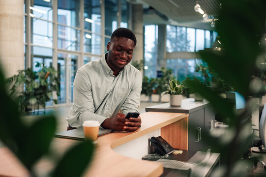 Young black man smiling using smartphone at office reception - Powered by Adobe