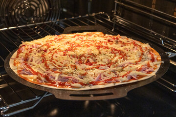 A large homemade pizza bakes on a round stone tray inside a kitchen oven, bubbling cheese and scattered toppings visible. Warm oven light highlights crust and melting cheese in a cozy scene.