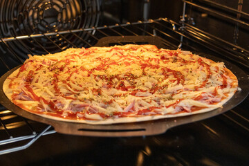 Close-up of a pizza cooking on a pizza stone in an oven, showing bubbling cheese and evenly spread toppings. Golden crust edges are visible as the pie bakes under warm interior oven light.